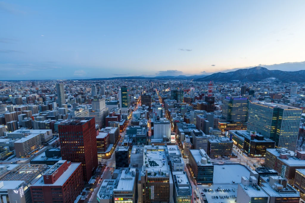 Vue aérienne de Sapporo au crépuscule en hiver, avec ses bâtiments enneigés et les montagnes en arrière-plan