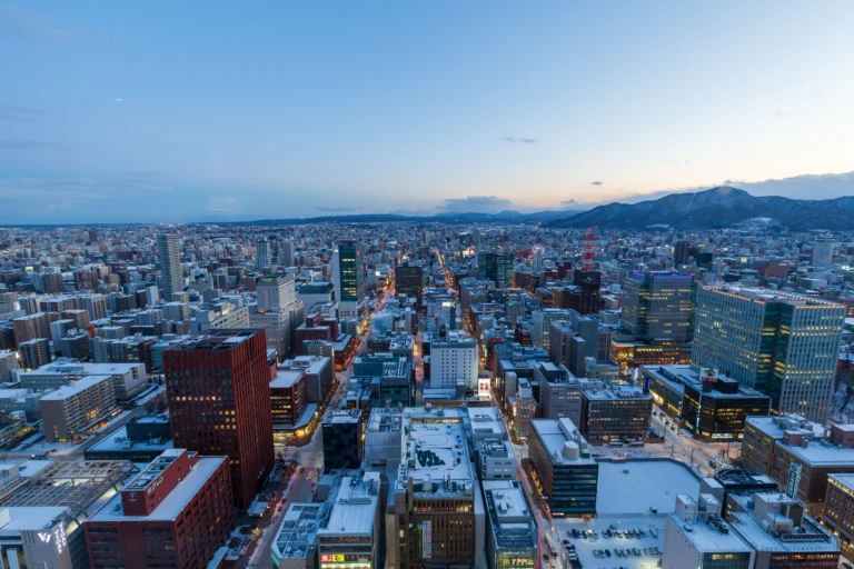 Vue aérienne de Sapporo au crépuscule en hiver, avec ses bâtiments enneigés et les montagnes en arrière-plan