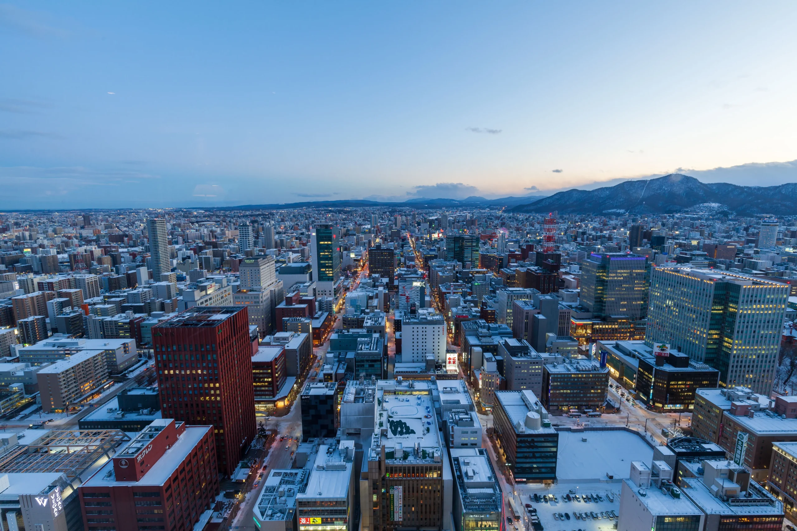 Vue aérienne de Sapporo au crépuscule en hiver, avec ses bâtiments enneigés et les montagnes en arrière-plan