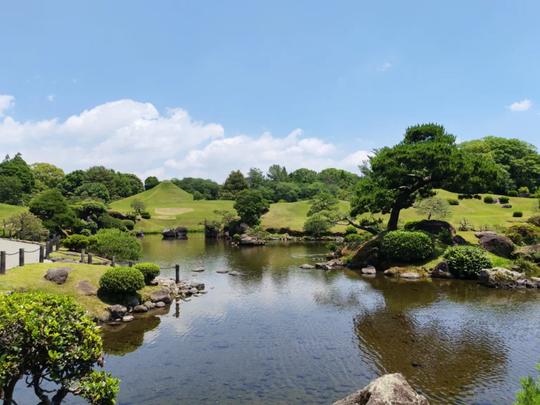 Parc verdoyant Suizen-ji joju-en avec ses arbres, arbustes, buissons et son étang sous le ciel bleu de Kumamoto