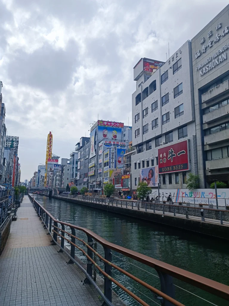 Promenade le long du canal de Dōtonbori à Osaka, entourée de bâtiments, de restaurants et des célèbres enseignes publicitaires du quartier